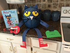 a blue cat sitting on top of a kitchen counter next to a book and toy guitar