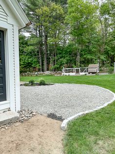 a graveled area in front of a house next to a lawn with chairs on it