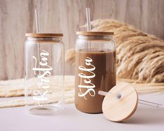 two personalized mason jars with lids and straws next to some dried grass on a table