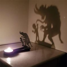 a shadow of a creature on a wall next to a lit candle and a small figurine