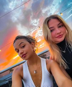 two young women sitting next to each other in front of an orange and blue sky