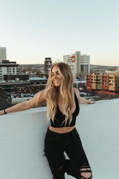 a woman leaning against a wall with her hands on her hips and looking at the camera