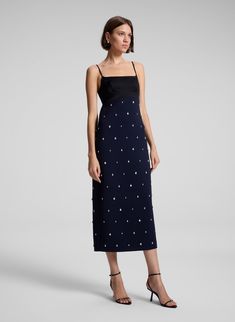 The Alana Dress combines deep rich navy cady fabric and black high-shine satin, adorned with scattered, teardrop-shaped crystals, offering a unique take on festive embellishment. This midi silhouette features a straight skirt, a bustier-inspired bodice with adjustable straps, and delicate side cutouts with an open back for a modern, striking look. Shop Dresses. Styling Tip: Pair with metallic heels and a sleek clutch for an elegant dinner or holiday soirée. Contrast Sequin Midi Dress For Gala, Evening Midi Dress With Contrast Sequin, Blue Embellished Midi Dress For Evening, Embellished Midi Length Evening Dress, Embellished Silk Midi Dress For Formal Occasions, Formal Embellished Silk Midi Dress, Chic Embellished Silk Midi Dress, Embellished Silk Midi Dress, Elegant Blue Embellished Midi Dress