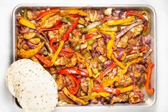 a pan filled with chicken and peppers next to a tortilla