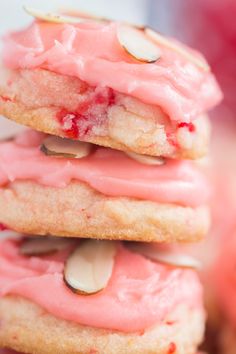 a stack of cookies with pink frosting and almonds