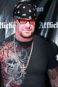 a man in black shirt and bandana standing next to a wall with skulls on it