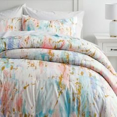 the comforter is made up with colorful paint splattered on it and white pillows