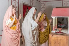 three people dressed as jesus and mary are standing in a room with red curtains on the walls