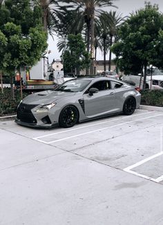 a silver sports car parked in a parking lot next to palm trees and bushes on a cloudy day