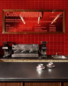 a coffee shop with red tile walls and black counter tops, two espresso machines on the wall