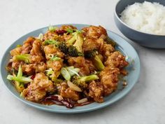 a blue plate topped with chicken and broccoli covered in sauce next to rice