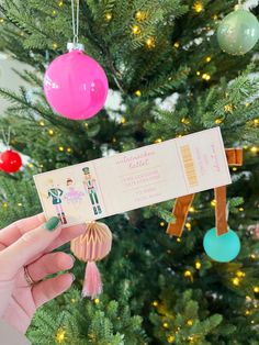 a person holding up a ticket in front of a christmas tree with ornaments on it