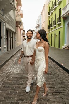 a man and woman are walking down the street holding hands while looking at each other