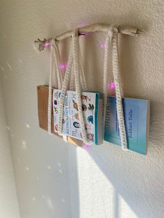 three books are hanging on the wall with string lights attached to each bookmarks