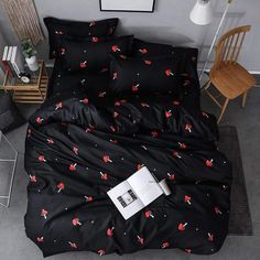 a black bed with red cherries on it in a room next to a chair