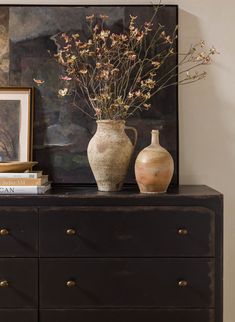 two vases with flowers sit on top of a dresser in front of a painting