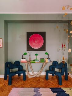 a living room with blue chairs and a painting on the wall above it's table