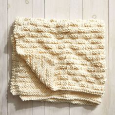 a white knitted blanket on top of a wooden floor