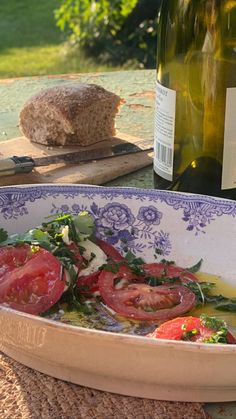 a bowl filled with tomatoes and greens next to a bottle of wine on a table