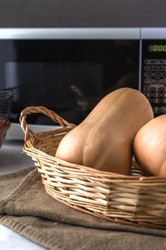 two butternuts sit in a basket next to a microwave