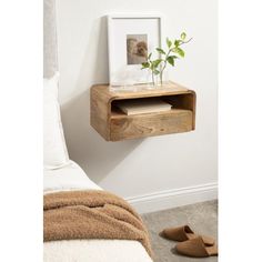 a small wooden shelf with a plant on it next to a bed and slippers