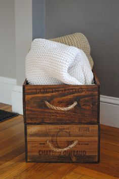 a wooden crate with white towels in it sitting on the floor next to a door