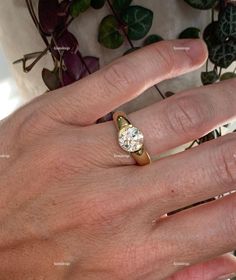 a person's hand with a ring on it and a plant in the background