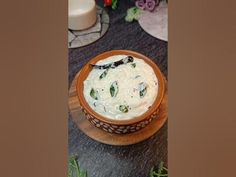 a wooden bowl filled with white sauce on top of a black table next to flowers