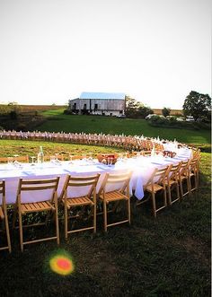 a long table is set up in the middle of a field for an outdoor dinner