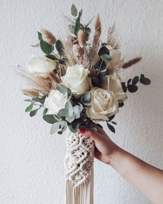 a person holding a bouquet of white roses and greenery in front of a wall