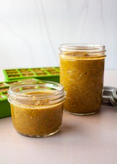 two jars filled with food sitting on top of a table next to a green box