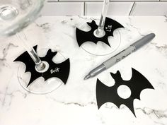 two wine glasses with bats on them sitting next to a glass filled with water and a pen