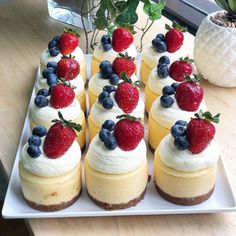 several desserts are arranged on a white platter with strawberries and blueberries