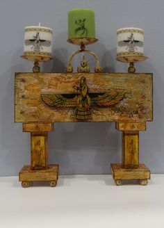 two candles are sitting on top of an old wooden box with egyptian designs and symbols