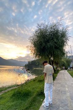 a man standing on the side of a road next to a tree and water at sunset