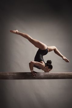 a woman in black leotard doing a handstand on a wooden beam