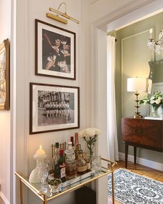 a bar cart with liquor bottles and glasses on it in front of two framed pictures