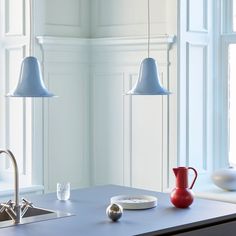 a kitchen island with two hanging lights above it and a red vase on the counter