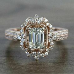 a fancy engagement ring with an emerald center surrounded by white and brown diamonds on a wooden surface