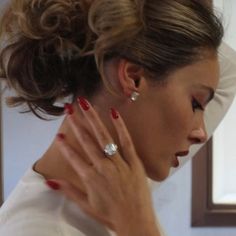 a woman with her hands on her neck looking down at the ground while wearing red nail polish