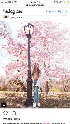 a woman standing next to a lamp post with pink flowers on the trees in the background