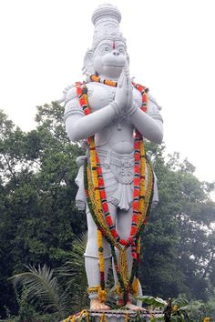 there is a large statue in the middle of some plants and trees with flowers all around it