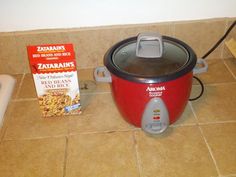 a red rice cooker next to a box of zara's cereal on the floor