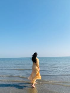 a woman in a yellow dress walking on the beach