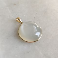 ITEM DESCRIPTION: >>The pendant is made from Solid 14K Yellow Gold. Gemstone used is absolutely natural and ethically sourced.  >>Natural White Moonstones cabochon cut and round shape with bezel setting are studded on it with utmost precision.  >>This is a minimalist design and is absolutely hassle-free and everyday jewelry.  ✓ Gem: White Moonstone ✓ Gem size: 25x25 mm round  ✓ Gem weight: 37.93 carats ✓ Gold purity: 14K (58.33% approx.) ✓ Gold weight: 0.81 grams  ✓ Gross weight: 8.40 grams The Gold purity is guaranteed and it comes with authentic 14K gold hallmark. Since these Pendants are handmade, they are Nickel/Lead FREE.  CUSTOMIZATION: --> You can choose your own gemstone as well. --> The same pendant can be made in thicker bezel as well. --> Kindly drop a message for the same. CUST White 14k Gold Jewelry With Round Stone, Elegant White Jewelry With Moon Phase Detail, Elegant White Moon Phase Jewelry, Gold Polished Moonstone Jewelry, Gold Moonstone Jewelry With Polished Finish, White 14k Gold Jewelry With Round Pendant, White Polished Finish Round Pendant Jewelry, Modern Yellow Gold Moonstone Jewelry, Elegant Chalcedony Jewelry With Polished Finish