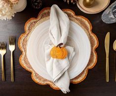 a place setting with gold and white plates, silverware and napkins on a wooden table