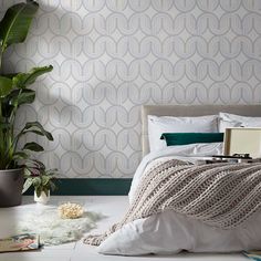 a bed with white sheets and pillows next to a potted plant on the floor