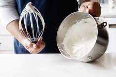 a person holding a whisk in a metal bowl on top of a counter