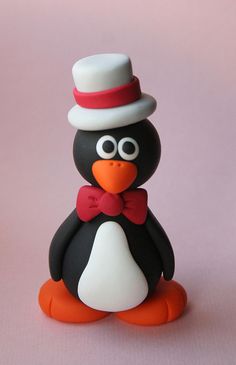 a penguin with a hat and bow tie sitting on a pink surface, looking at the camera