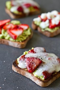 four pieces of toast with strawberries and avocado on them sitting on a table